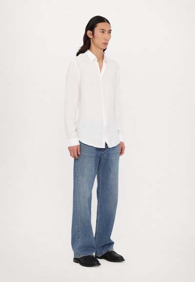 White long-sleeve linen shirt, relaxed fit, paired with loose blue denim jeans. Black shoes complete the outfit. Simple, casual design.