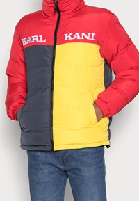 Giubbotto imbottito rosso, grigio e giallo con chiusura a zip, due tasche laterali, polsini a costine e logo sul petto. Tessuto trapuntato.