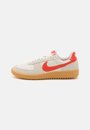 Hvid og beige sneaker med gummisål, rød Nike-swoosh og hæftelap ved hælen, hvide snørebånd og polstret krave, vist fra ydersiden.