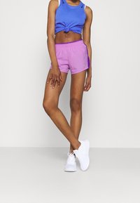 Lila och rosa sportshorts med resårmidja, tillsammans med en blå melerad tanktop och vita löparskor.