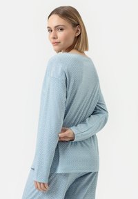 Ensemble loungewear bleu clair avec un motif en losange, des manches longues et une coupe décontractée. Le haut a un col rond et une texture côtelée subtile.