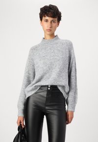 Light gray, fuzzy knit sweater with a high neck and long sleeves, paired with black, shiny, form-fitting pants.