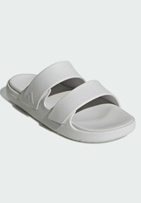Vaaleanharmaat liukusandaalit, joissa on kaksi leveää hihnaa, pehmeä pinta ja korotettu pohja mukavuutta varten. Sivussa on hienovarainen logo.