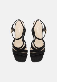 Sandali con tacco alto in suede nero, design con cinturini incrociati, punta aperta e cinturino alla caviglia con dettaglio di fibbia dorata.