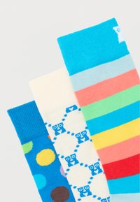 Τρεις πολύχρωμες κάλτσες με σχέδια: μπλε με πολύχρωμες τελείες, κρεμ με μπλε αρκουδάκια και ρίγες σε χρώματα του ουράνιου τόξου.