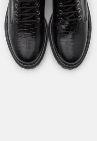 Bottes en cuir noir embossé effet crocodile avec bouts ronds, six œillets, lacets noirs et semelle en caoutchouc texturée.