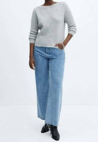 Grau gerippter Pullover mit Dreiviertelärmeln, kombiniert mit weit geschnittenen, hellblauen Jeans. Schwarze Stiefeletten runden das Outfit ab.