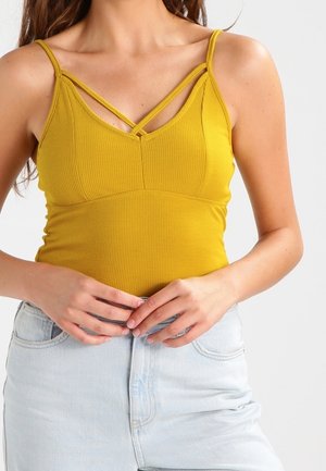 Żółty prążkowany top na ramiączkach z dekoltem w kształcie litery V i skrzyżowanymi ramiączkami. Połączony z niebieskimi szortami z wysokim stanem.