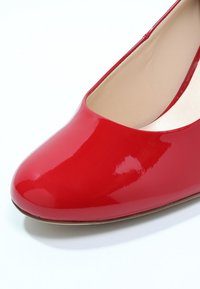 Chaussure plate en cuir verni rouge avec un bout arrondi, une surface lisse et une doublure intérieure de couleur claire. Design simple, sans éléments métalliques visibles ni motifs.