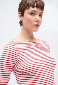 Piros-fehér csíkos, hosszú ujjú felső hajónyakánál, sima, rugalmas anyagból. Testhez simuló fazonú, finom vállvarrás részletekkel.