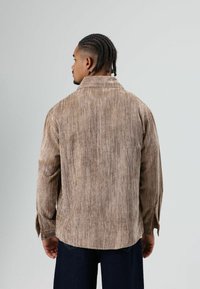 Brown corduroy shirt with a soft texture, long sleeves, and a straight-cut hem. Features a standard collar and side slits at the cuffs.