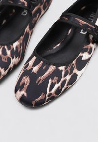Schwarze flache Schuhe mit einem Leopardenmuster in Brauntönen und Creme. Mit einer runden Zehenpartie und einem schwarzen elastischen Riemen über dem Spann.