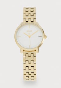 Montre en métal doré avec un cadran blanc, présentant un design simple, des index horaires et un bracelet à maillons. Nom de la marque affiché en évidence.