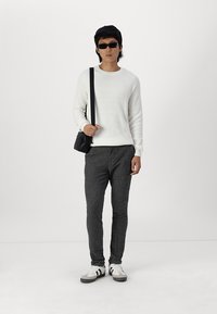 Suéter blanco de canalé, pantalones grises con textura, bolso cruzado negro, gafas de sol negras y zapatillas blancas con detalles negros.