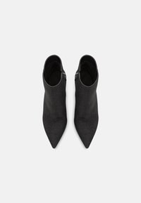 Botines negros y puntiagudos con parte superior de tela elástica y detalle de cremallera en el lateral, con una textura elegante y suave.