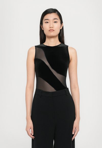 Bodysuit noir avec un design en panneau en maille transparente. Il présente une coupe sans manches, un col arrondi et une texture lisse, associé à un pantalon noir taille haute.