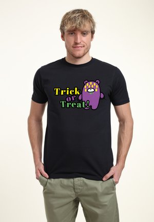 Hombre con camisa negra con texto colorido "Trick or Treat" y un monstruo de dibujos animados púrpura con manchas amarillas en el pecho.