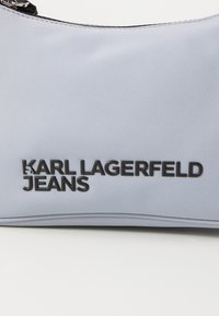 Šviesiai mėlynas sintetinis maišelis su įspaustu juodu prekės ženklu "KARL LAGERFELD JEANS." Turi lygų paviršių ir išlenktą formą su užtrauktuko uždarymu.