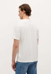 T-shirt en coton blanc à col rond et manches courtes, avec une coupe droite et une petite étiquette logo à l'ourlet, associé à un jean bleu.