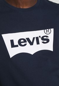 T-shirt in cotone blu navy con logo Levi's bianco caratterizzato da un distintivo contorno rosso curvo, che mette in risalto una tipografia audace.