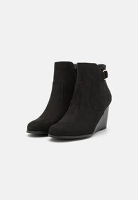 Bottines en suede noir avec un talon compensé, dotées d'une fermeture éclair sur le côté et d'une boucle décorative. Texture lisse et lignes épurées.