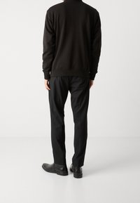 Černá mikina s kulatým výstřihem a žebrovanými manžetami, doplněná o černé úzké kalhoty a pevné černé boty.