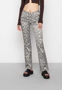 Spodnie flare z nadrukiem w wężową skórę w kolorze srebrnym i czarnym, charakteryzujące się gładką teksturą i dopasowanym pasem. Noszone z czarnymi sandałami na platformie.