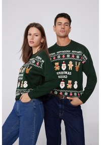 Les pulls de Noël en maille verte présentent des motifs festifs, incluant des bonhommes de neige, des rennes et le texte "Christmas Squad". Poignets et encolure côtelés.