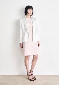White blazer over a light pink fitted dress, paired with black strappy heels. Smooth fabric, tailored design, and minimalistic details.