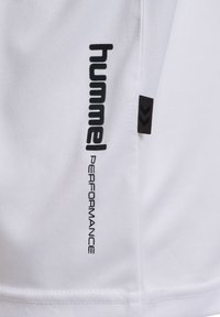 Vita sportshorts i lättviktsmaterial med svart "hummel"-logotyp och texten "PERFORMANCE", med en svart accenttagg på sidan.
