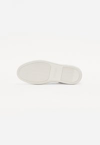 Semelle de chaussure avec une surface en caoutchouc blanc lisse, présentant un motif en zigzag et un logo en relief. orteil arrondi et design minimaliste.