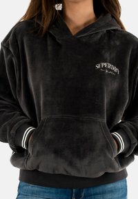 Zwarte ribfluwelen hoodie met een kangoeroezak, geribde manchetten met witte strepen en een logo in witte stiksel op de borst.