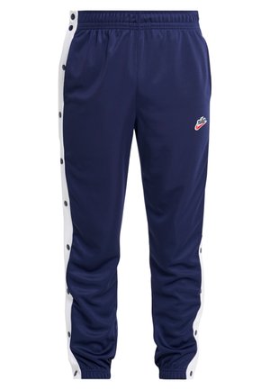 Granatowe spodnie dresowe z białymi bocznymi paskami zapinanymi na zatrzaski i logo Nike na lewym udzie, z elastycznym pasem i ściągaczami.