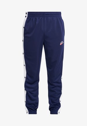 Granatowe spodnie dresowe z białymi bocznymi paskami zapinanymi na zatrzaski i logo Nike na lewym udzie, z elastycznym pasem i ściągaczami.