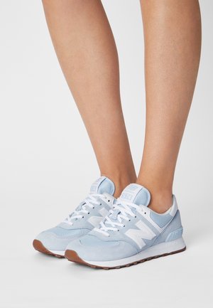 Zapatillas deportivas de ante azul claro y malla con detalles blancos, con diseño de cordones y suela de goma. Número de modelo "574" visible en la lengüeta.