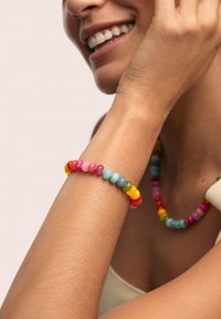 Colorful beaded bracelet featuring rounded beads in pink, yellow, blue, green, and orange, worn on a bare wrist against a neutral background.