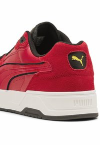 Sneaker rossa realizzata con materiali in pelle e suede, dettagli neri, suola bianca e logo Puma giallo sul tallone. Presenta una forma arrotondata con cuciture.