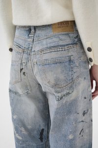 Ανοιχτό μπλε τζιν παντελόνι με ξεθωριασμένη, φθαρμένη όψη, με πολλαπλά σημάδια φθοράς, καφέ λογότυπο και κλασικό σχέδιο με πέντε τσέπες.