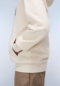 Crème kleurige hoodie met ribgebreide manchetten en zak. Zachte stof, losse pasvorm, met een minimalistisch ontwerp. Subtiele naaddetails zichtbaar.