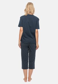 Marinblå bomulls t-shirt med korta ärmar, i kombination med svarta och vita randiga capribyxor, som har en avslappnad passform och längd mitt på vaden.
