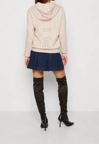 Ljusrosa hoodie med en stor grafik på baksidan, tillsammans med en denimveckad kjol och svarta höga stövlar med klack. Släta texturer.