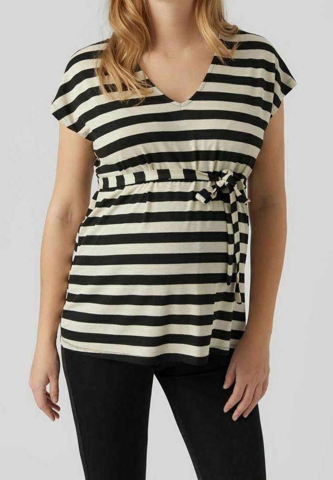Femme portant un haut rayé noir et blanc à col en V, manches courtes, avec une ceinture nouée sur un pantalon noir.
