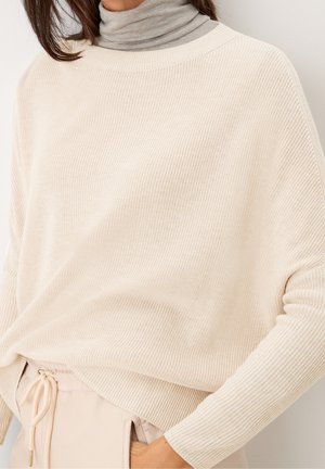 Maglione beige a coste, con scollo ampio e spalle scese, indossato sopra un dolcevita grigio chiaro. Tessuto morbido con una vestibilità comoda.