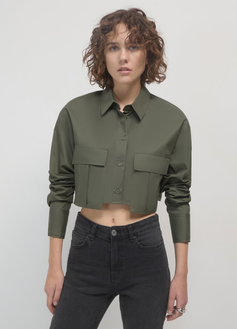 Chemise boutonnée, couleur vert olive, à manches longues et deux poches poitrine, fabriquée en tissu lisse avec une finition brillante.