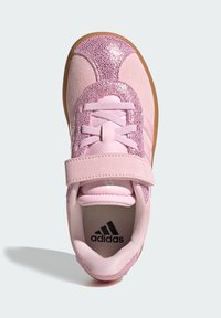 Pink athletic shoe with a glittery upper, suede toe cap, and adjustable strap. Features cushioned insole and rubber outsole.