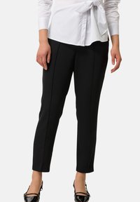 Czarne spodnie o dopasowanym kroju wykonane z elastycznego materiału, z detalami w postaci zaszewek z przodu, zestawione z czarnymi lakierowanymi balerinami.