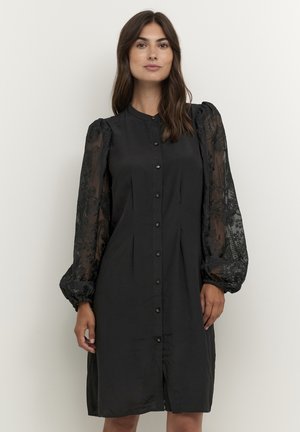 Robe noire avec un devant boutonné, un design plissé et des manches bouffantes en dentelle transparente à motifs floraux. Texture de tissu lisse.