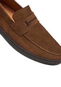 Braune Wildlederloafers mit glatter Oberfläche, blunted Zehenform und schwarzer Gummisohle. Merkmale sind ein auffälliges, gestepptes Riemendetail auf dem Obermaterial.