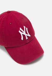Rode katoenen baseballcap met een gebogen rand, voorzien van een witte geborduurde 'NY' logo aan de voorkant en ventilatiegaten op de kroon.