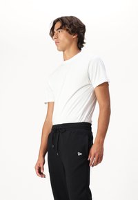Witte katoenen T-shirt met korte mouwen, gecombineerd met zwarte sweatpants met trekkoord en een klein wit logo op de linkerbovenbeen.